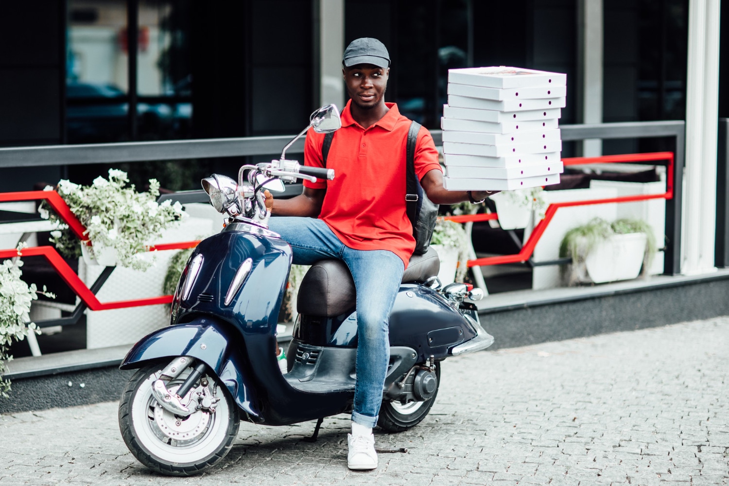 motoboy sentado na moto tentando equilibrar várias caixas de pizza