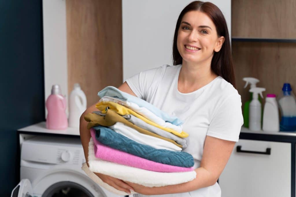 mulher sorridente segura pilha de roupas limpas numa lavanderia