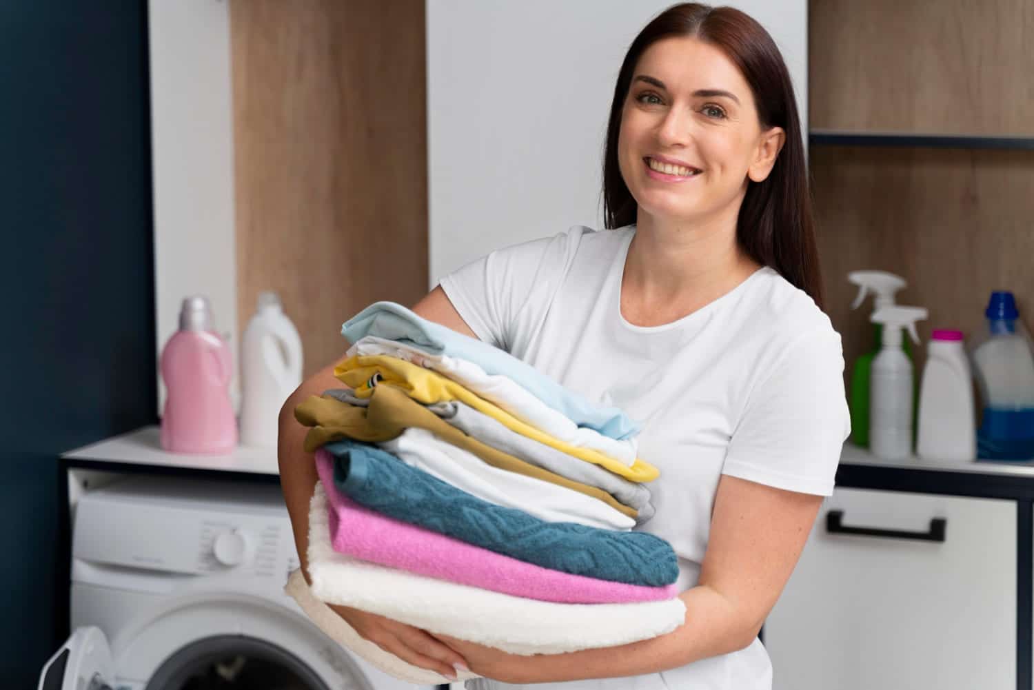 mulher sorridente segura pilha de roupas limpas numa lavanderia